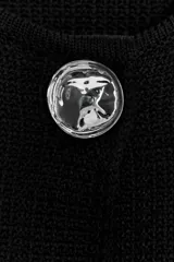 Chaqueta corta negra de tejido texturizado, con cuello redondo y manga ancha tipo kimono que termina por debajo del codo. Cierre frontal con un único botón joya metálico plateado con relieve.