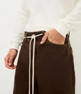 Pantalón masculino de corte baggy, confeccionado en sarga de algodón. Presenta un diseño holgado con costuras en contraste, cierre tradicional y cordón ajustable en la cintura.