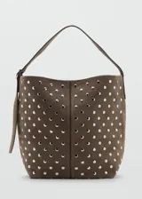 Bolso tipo hobo de cuero gamuzado color marrón, con diseño de tachas metálicas plateadas distribuidas por toda la superficie. Cuenta con una correa de hombro integrada y cierre superior.