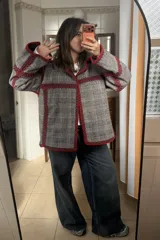 Chaqueta reversible de paño, con un lado gris oscuro con costuras decorativas en hilo rojo y el otro lado con estampado de cuadros. Presenta corte holgado, mangas largas y diseño abierto.