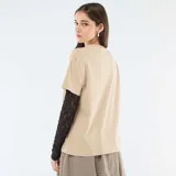 Camiseta de manga corta color beige con estampado gráfico frontal en negro, que incluye una segunda capa de mangas largas de encaje negro debajo.