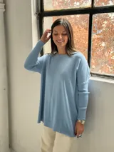 Sweater de punto color celeste, con cuello redondo, corte holgado y mangas largas con puños acanalados. Presenta un detalle de costura vertical central en el frente.