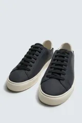 Zapatilla de cordones color negro con parte superior lisa, horma redonda y forro interior a contraste. Suela de goma color crema con ligera textura y detalle en el talón color crema.