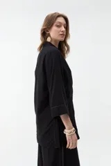 Blazer negro de corte recto y holgado, con doble botonadura frontal, solapas clásicas y mangas tres cuartos con costuras pespunteadas en contraste.