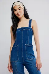 Mameluco de denim elastizado azul, entallado en el cuerpo con pierna bootcut. Presenta escote cuadrado, bolsillos plaqué delanteros, tiras anchas y cierre en la espalda.
