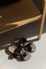 Sandalias bajas de cuero color beige con doble tira de cuero negro con textura y hebilla metálica.