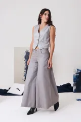 Pantalón tipo palazzo de tiro medio, confeccionado en denim de algodón con acabado metalizado plateado. Presenta cierre frontal con botón metálico, bolsillos laterales y traseros, y una silueta de pierna ancha muy amplia.