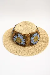 Sombrero de ala ancha color tostado, tejido en papel con detalles de apliques de crochet en la parte central con diseño de flores en tonos celestes, marrones y verde oliva.