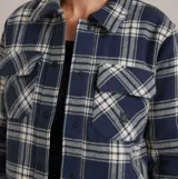 Campera tipo sobrecamisa de corte cropped, confeccionada en tela de franela con diseño de cuadros en tonos azul marino y crema. Presenta cuello clásico, cierre frontal con botones, bolsillos con solapa en el pecho y forro interior acolchado.