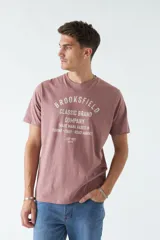 Remera color ladrillo con estampado frontal con la leyenda "BROOKSFIELD CLASSIC BRAND COMPANY TRADE MARK BASED IN TORINO - ITALY - ROAD MARKET EST 1971 REG TM".