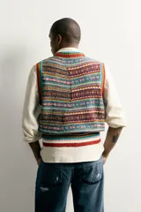 Chaleco de punto tejido en hilatura de algodón con diseño patchwork de patrones jacquard multicolores, cuello redondo y terminaciones en rib.