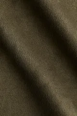 Camisa corta color verde militar, de corte holgado, con cuello clásico, botones frontales y canesú en la espalda. Presenta hombros caídos y mangas largas con puños anchos.