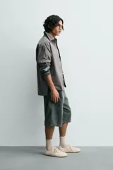 Camisa blanca de algodón con corte relajado, cuello solapa, manga larga con puño abotonado y bolsillo de plastrón en el pecho. Presenta bajo asimétrico con aberturas laterales y cierre frontal de botonadura.