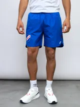 Short deportivo azul con escudo del Club Nacional de Football en la pierna derecha y detalles tricolor.