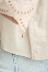 Blusa color arena de algodón peinado, con escote redondo, mangas cortas abullonadas con bordados suizos y detalles de alforcas en el frente.