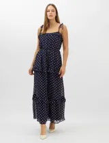 Vestido largo azul marino con estampado de lunares blancos, confeccionado en gasa fluida. Cuenta con tirantes finos ajustables con lazos en los hombros, escote con volados, corte en la cintura con lazo ajustable, y falda larga con múltiples capas y volados horizontales.