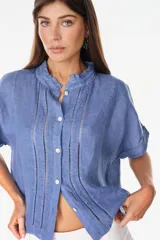 Camisa azul de lino italiano, de corte suelto y mangas cortas, con cuello mao con volados y detalles de calados verticales en el frente.