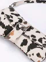 Cartera baguette con estampado de vaca en blanco y negro, con correa de hombro y cierre con hebilla metálica.