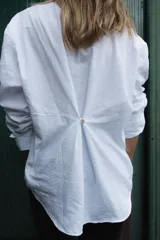 Camisa de algodón color marrón con corte clásico y cuello camisero. Presenta un bordado geométrico en color negro en la parte frontal y mangas largas con puños abotonados.