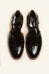 Sandalia cerrada tipo pescador de cuero negro charol, con tira en T y hebilla ajustable en el tobillo. Posee suela y taco bajo de madera.