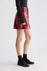 Minifalda evasé de tiro alto, confeccionada en material sintético de acabado brillante, estilo charol, con diseño de cinco bolsillos y cierre frontal con botón y cremallera.