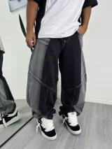 Pantalón de jean estilo baggy con diseño de paneles en contraste de color negro y gris lavado. Presenta costuras visibles, corte holgado y diseño de pierna ancha.