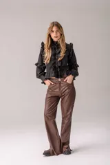 Camisa negra de corte entallado con volados decorativos en el cuello, la botonadura frontal, los hombros y las mangas. Presenta mangas largas con puños ajustados y un ruedo con volado inferior.