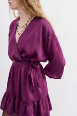 Vestido corto de estilo cruzado, color negro, con mangas largas abullonadas, puños elásticos y volado en el ruedo. Presenta un diseño de jacquard con corazones y cierre frontal con botones metálicos.