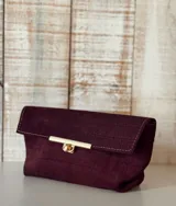 Sobre de mano tipo clutch en color bordó, con textura de efecto cocodrilo y acabado en gamuza. Presenta un cierre frontal metálico en tono dorado con diseño de barra y broche giratorio.