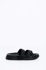 Sandalias negras de doble tira con tachas doradas, suela plana y diseño cómodo.