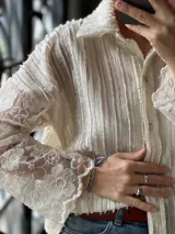 Camisa blanca de manga larga con diseño texturizado en el cuerpo y mangas de encaje con motivo floral translúcido, cuello camisero y cierre frontal con botones.