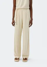 Pantalón de corte recto color beige con pinzas en la parte delantera y tira ajustable a modo de cinturón con nudos decorativos.