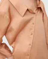 Vestido camisero midi de tejido satinado en tono salmón, con cuello italiano desestructurado, mangas largas con puños abotonados y una original botonadura frontal asimétrica.