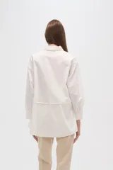 Camisa blanca de algodón, holgada, con cuello camisero, cierre frontal con botones y mangas largas.