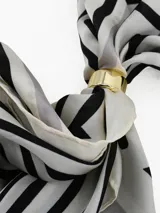 Pañuelo cuadrado de tela ligera color negro con estampado de lunares blancos y borde con franja blanca. Incluye un anillo metálico dorado para sujetar y estilizar el pañuelo.