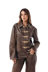 Campera estilo militar napoleón confeccionada en cuero ovino, con cierre frontal y solapa decorativa con botones metálicos y alamares de gamuza en tono crudo. Cuenta con cuello camisero, pespuntes visibles y diseño estructurado de manga larga.