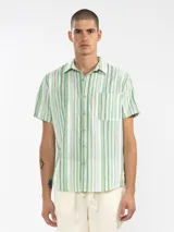 Camisa de manga corta con rayas verticales en tonos verde, gris y blanco. Tiene corte cuadrado, calce relajado, botones de coco con logo y un bolsillo en el pecho.