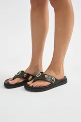 Ojotas de dedo negras con suela plana y gruesa, decoradas con apliques metálicos de piedras de colores en la tira.