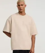 Remera oversized color beige confeccionada en gamuza sintética. Presenta cuello redondo, mangas cortas y bordado de cruz en el frente.