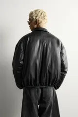 Cazadora acolchada relaxed fit de efecto piel en color negro, con cuello camisero, cierre frontal de cremallera metálica, bolsillos frontales de vivo y puños elásticos.