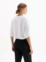 Remera blanca de corte cropped y manga corta, confeccionada en algodón. Presenta una estampa frontal con un conejo con estampado animal print sobre una nube y el texto 'IL BUNNY' en color amarillo.