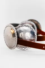 Cinturón marrón de cuero con apliques metálicos plateados de forma ovalada con borde irregular.