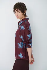 Camisa de corte clásico con cuello camisero y cierre frontal de botones, confeccionada en tela color bordó con estampado floral en tonos celestes.