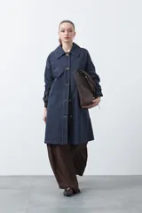 Trench azul marino de corte recto y largo midi, con costuras a la vista en color blanco, cuello camisero, cierre frontal con botones y mangas largas con trabillas ajustables en los puños.