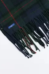 Bufanda de estilo escocés con diseño de cuadros en tonos verde, azul y líneas finas en rojo. Presenta flecos en los extremos y una etiqueta pequeña de la marca.
