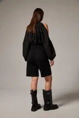 Bermuda de jean negro, de calce bajo y corte ancho a la rodilla, con tachas metálicas plateadas distribuidas por toda la prenda.
