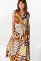 Blusa cruzada sin mangas confeccionada en algodón liviano, con cierre de lazo lateral en la cintura y cuello camisero. Presenta un diseño de rayas verticales y diagonales en tonos marrones, blancos y celestes.