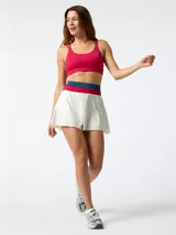Skort deportivo blanco con pretina ancha tejida en colores fucsia y azul. Cuenta con short incorporado en el interior y diseño plisado central, inspirado en el estilo de tenis vintage.