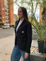 Blazer negro de tejido de punto en algodón, con solapas, dos bolsillos frontales y un escudo bordado en el pecho. Corte recto y holgado.