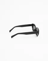 Lentes de sol negros con montura gruesa y forma ligeramente alargada y curvada, estilo 'cat eye' moderno. Los cristales son oscuros y polarizados.